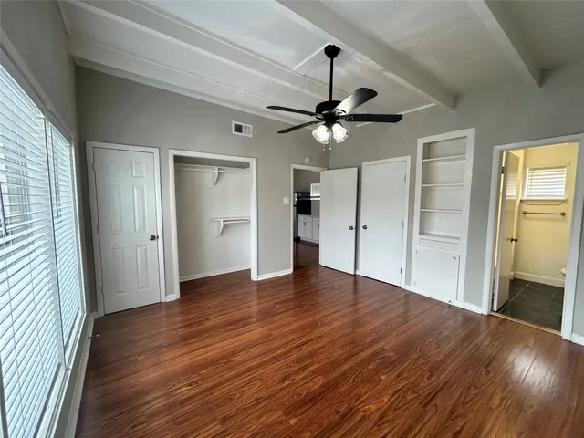 an empty room with wooden floor fan and windows