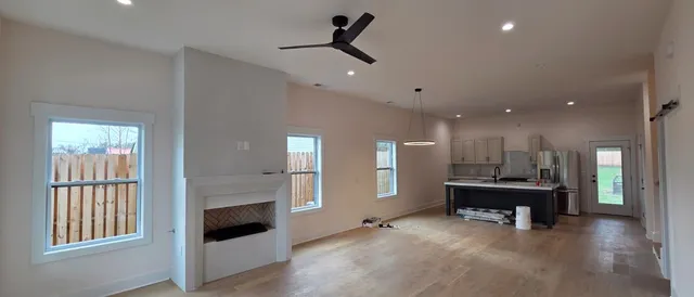 a view of an empty room with kitchen and fireplace
