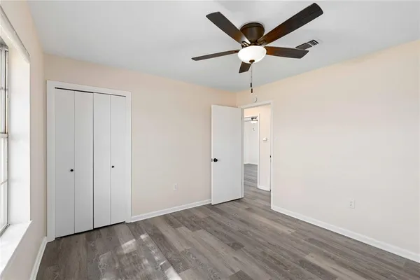 an empty room with wooden floor ceiling fan and window