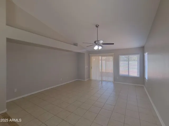 an empty room with chandelier fan and windows