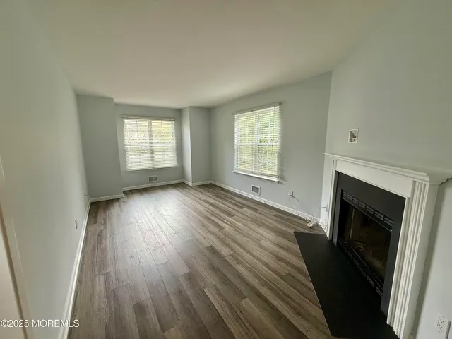 an empty room with wooden floor fireplace and windows