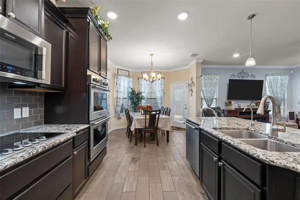 a kitchen with stainless steel appliances granite countertop a stove top oven a sink dishwasher a dining table and chairs with wooden floor