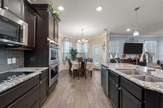 a kitchen with stainless steel appliances granite countertop a stove top oven a sink dishwasher a dining table and chairs with wooden floor