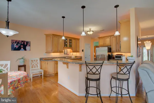 a kitchen with stainless steel appliances granite countertop a refrigerator a stove a sink a dining table and chairs with wooden floor