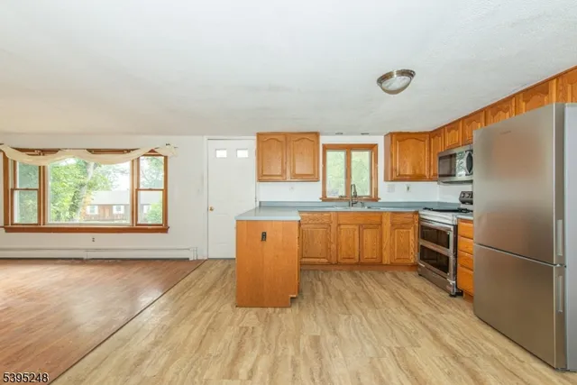 a kitchen with stainless steel appliances granite countertop a refrigerator a sink dishwasher a stove and white countertops with wooden floor