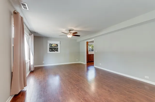an empty room with wooden floor chandelier fan and windows