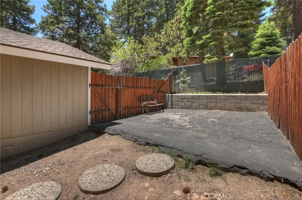 a view of a small house with wooden fence and large trees