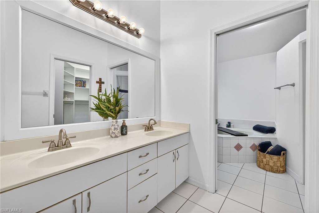 390 St Andrews Boulevard Naples, FL 34113 - Photo 18 of 42 Bathroom featuring double vanity, a bath, light tile patterned flooring, and a walk in closet