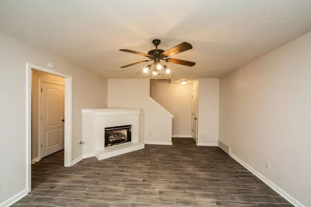 a view of an empty room with chandelier fan and fire place
