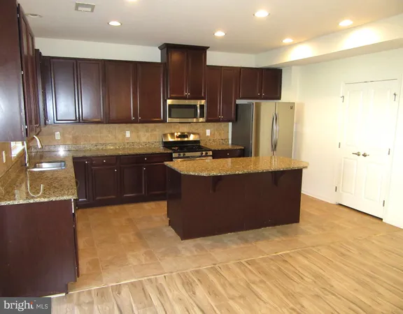 a large kitchen with kitchen island granite countertop wooden cabinets a refrigerator a stove a sink and dishwasher with wooden floor