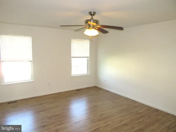 an empty room with wooden floor windows and fan