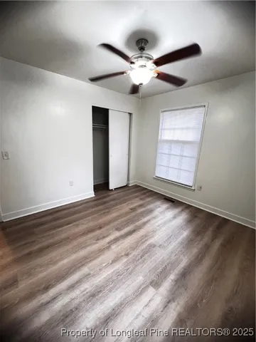 an empty room with wooden floor chandelier fan and windows