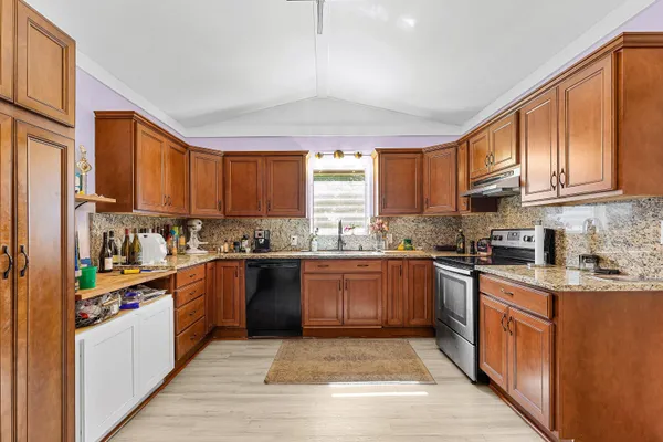 a kitchen with stainless steel appliances granite countertop wooden cabinets a stove top oven a sink and dishwasher with wooden floor