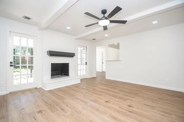a view of a livingroom with a fireplace a ceiling fan and wooden floor