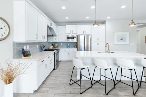 a kitchen with stainless steel appliances kitchen island granite countertop a refrigerator a stove a sink and white cabinets with wooden floor