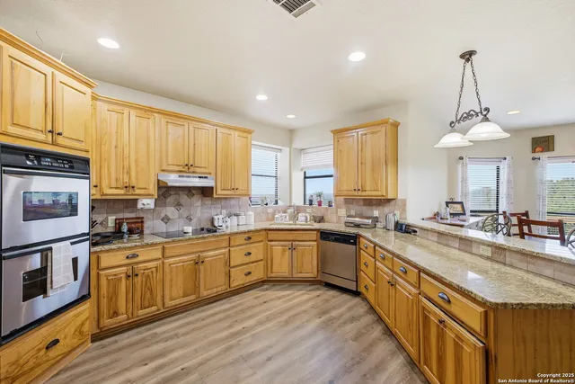 a kitchen with stainless steel appliances granite countertop a refrigerator a sink dishwasher a stove and a dining table with wooden floor