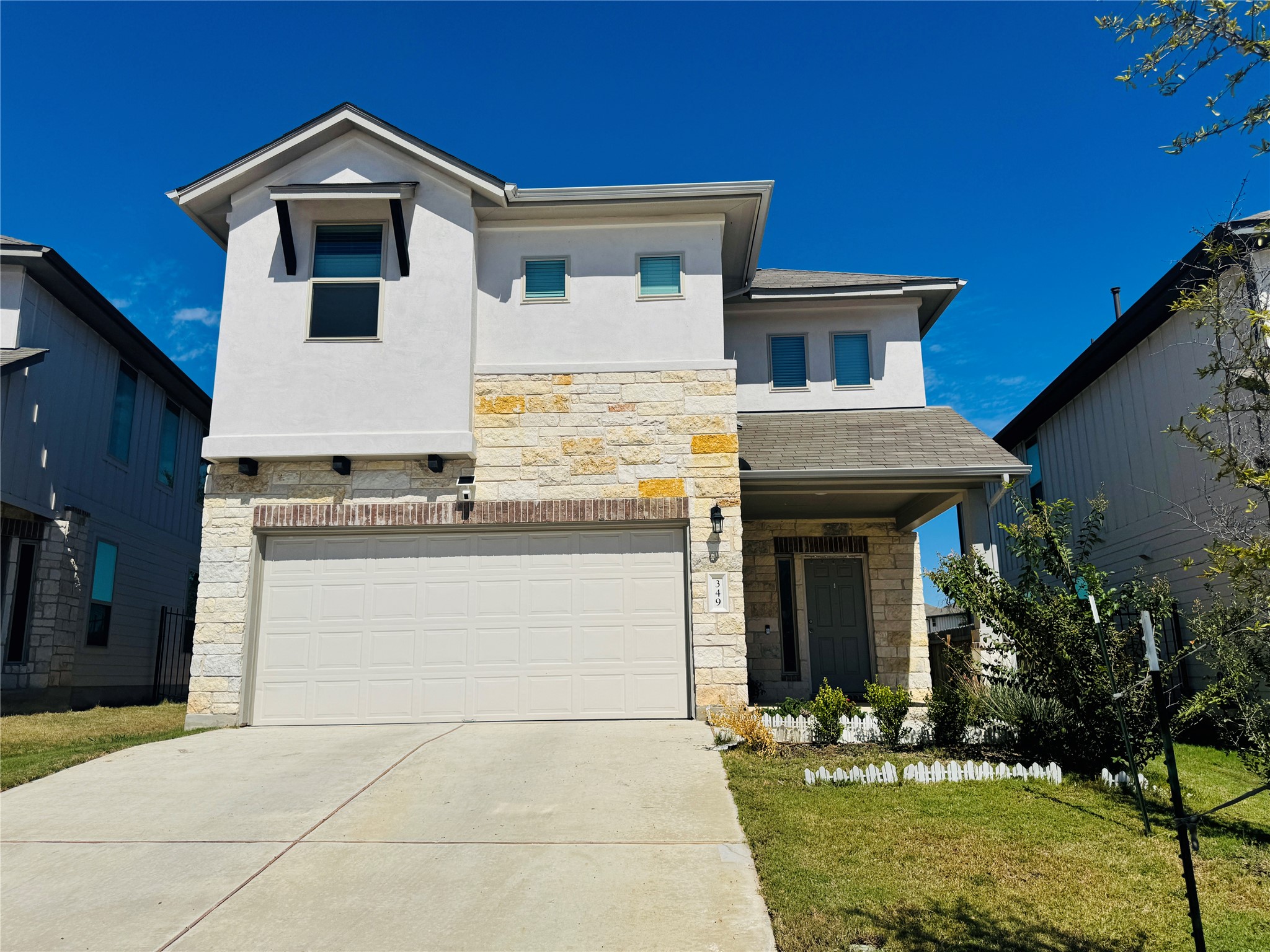 View of front facade with stone siding, a garage, stucco siding, and a front lawn