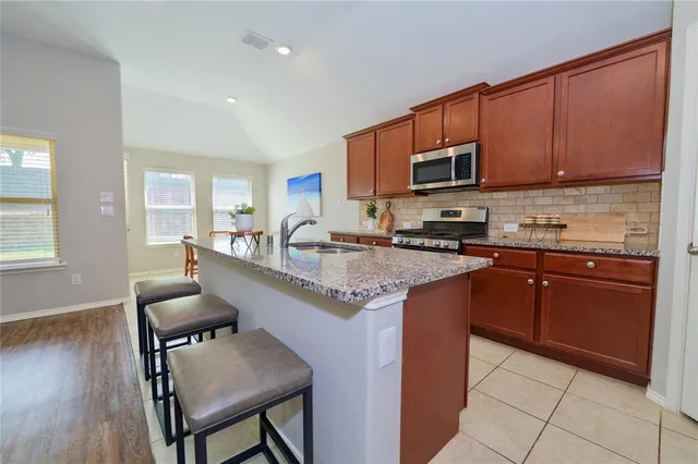 a kitchen with stainless steel appliances granite countertop a stove top oven a sink dishwasher a dining table and chairs with wooden floor