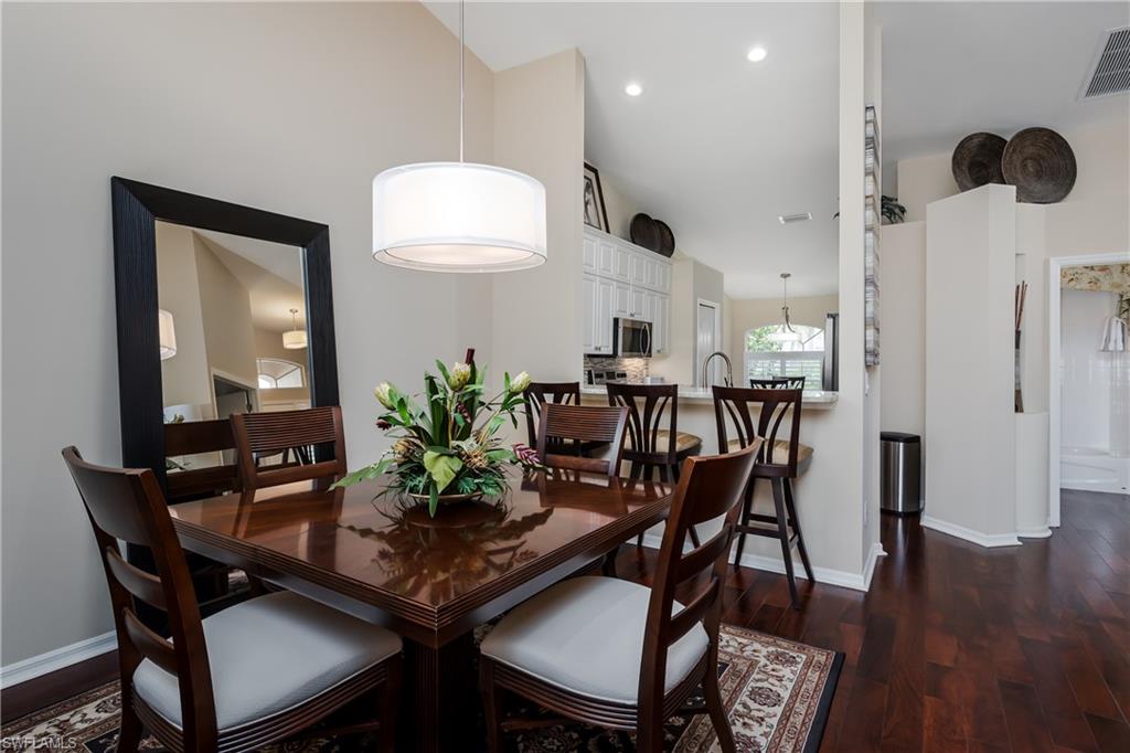 6658 Castlelawn Place, Unit 9 Naples, FL 34113 - Photo 11 of 38 Vaulted ceiling above a dining area featuring hardwood flooring, an arched window with white plantation shutters, and a contemporary drum pendant light fixture