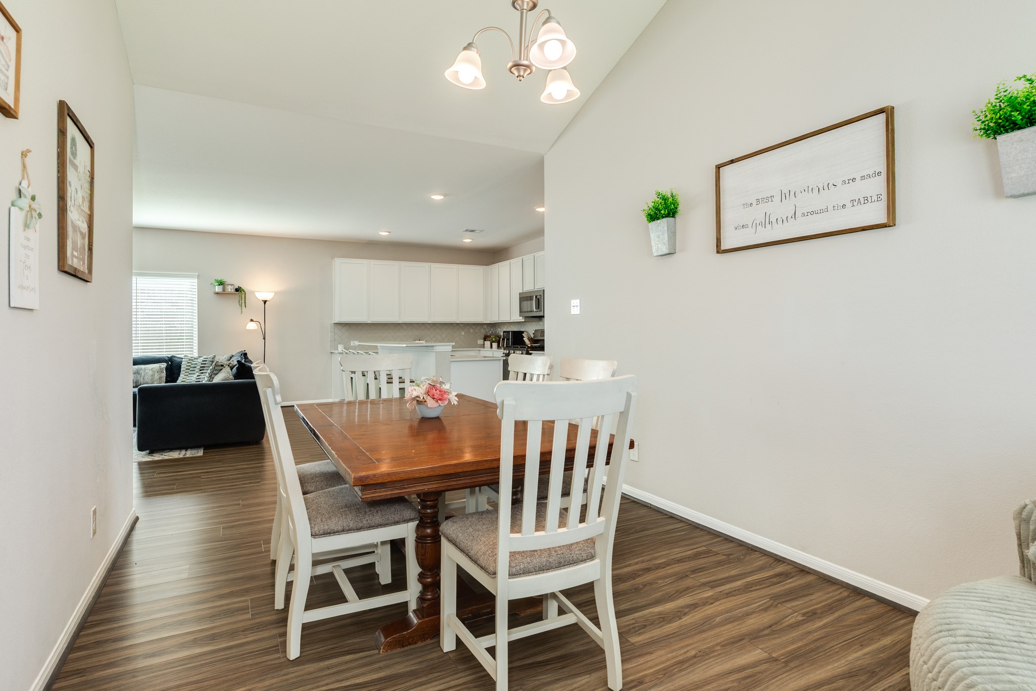 2446 Palisade Crst Drive Rosharon, TX 77583 - Photo 14 of 30 This photo showcases a bright, open-concept dining area with space for a large wooden table and white chairs, leading into a modern kitchen with white cabinetry. The space features light walls, wood look flooring, and tasteful decor, creating a welcoming atmosphere.