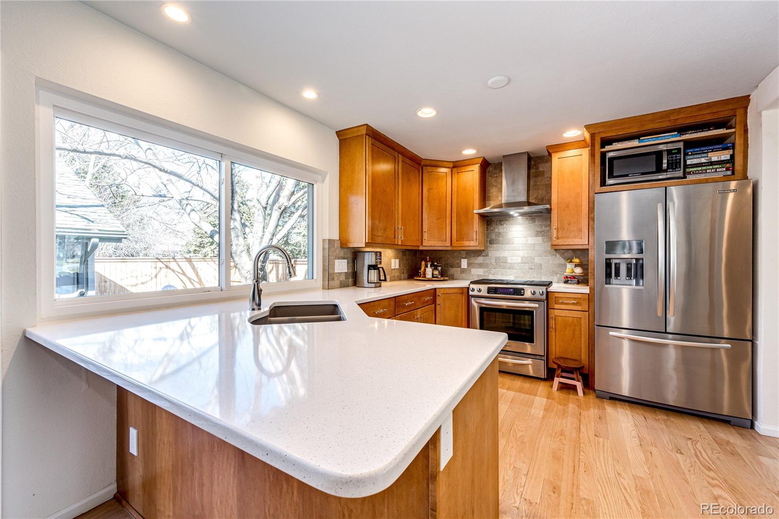 8712 Independence Way Arvada, CO 80005 - Photo 7 of 40 a kitchen with stainless steel appliances granite countertop a refrigerator a sink dishwasher a stove and white countertops with wooden floor