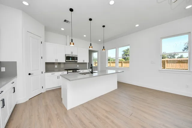 a large kitchen with stainless steel appliances kitchen island granite countertop a stove a sink a refrigerator and white cabinets with wooden floor