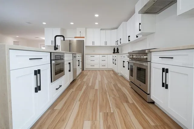 a kitchen with stainless steel appliances kitchen island granite countertop a stove a sink a refrigerator and white cabinets with wooden floor