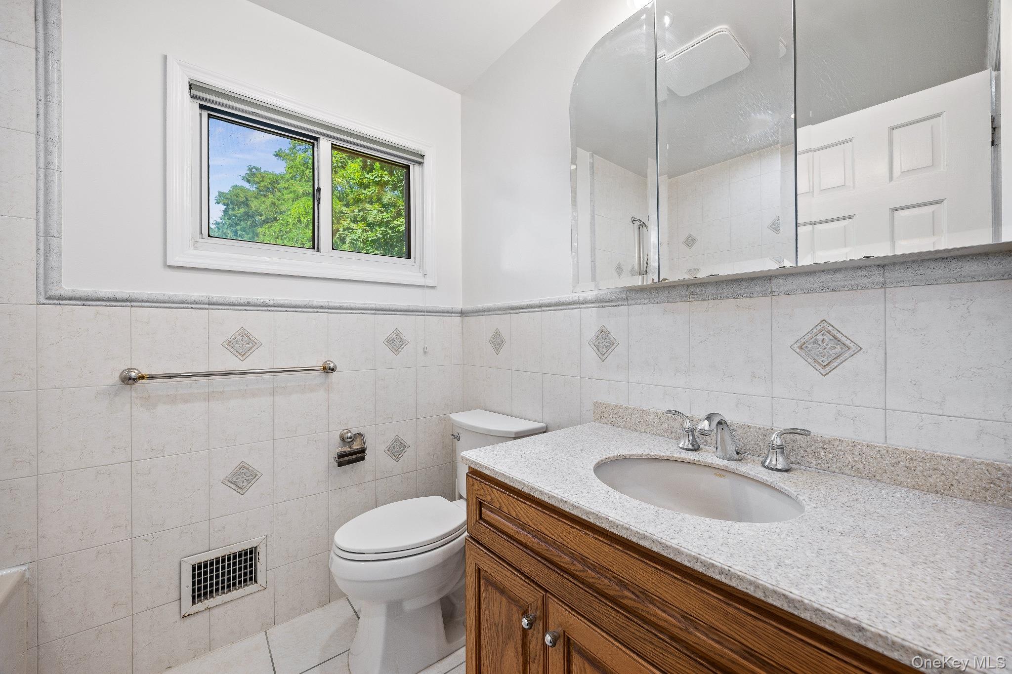 372 Heathcote Road Scarsdale, NY 10583 - Photo 13 of 20 Bathroom featuring vanity, tile walls, tile patterned floors, tiled shower, and a wainscoted wall