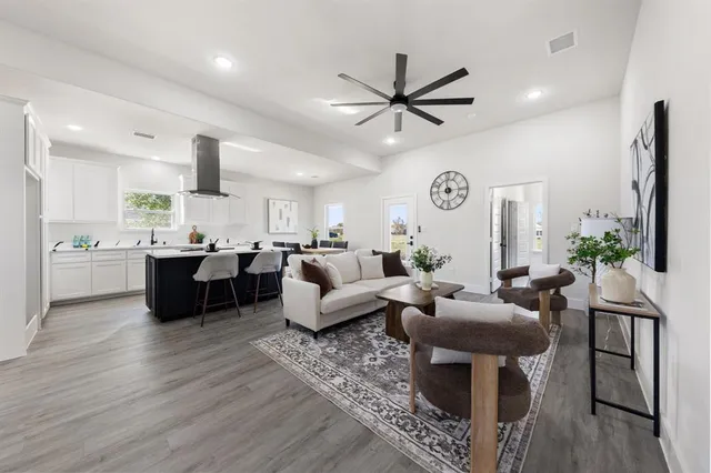 a living room with couches a fireplace and kitchen view with wooden floor