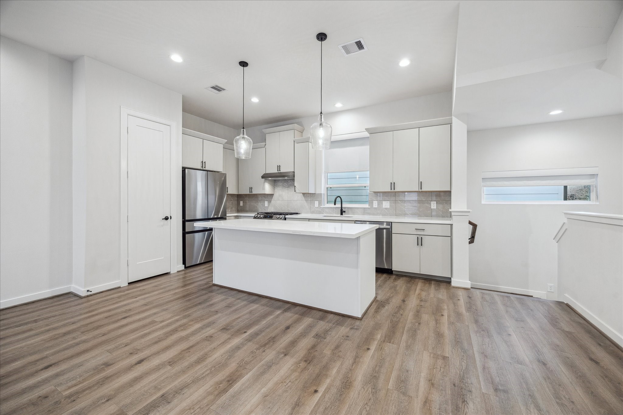 1603 Patterson Street, Unit E Houston, TX 77007 - Photo 11 of 32 This modern kitchen features sleek white cabinetry, stainless steel appliances, and a central island with pendant lighting. The open layout and wood-look flooring create a warm, inviting space perfect for cooking and entertaining.