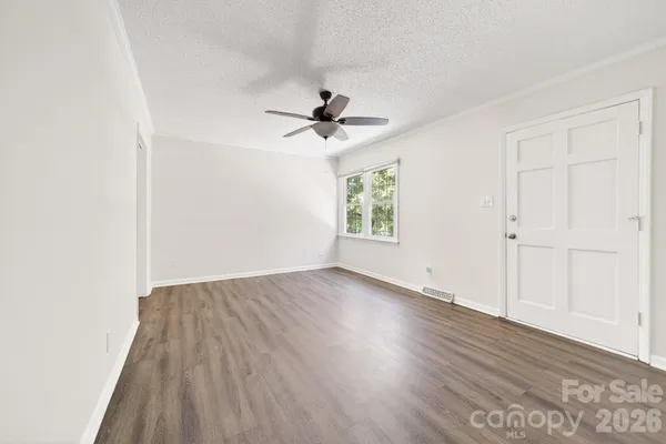 an empty room with wooden floor chandelier fan and windows