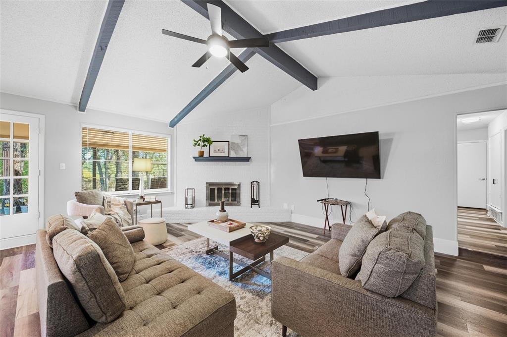 608 Ridgewood Circle Hurst, TX 76054 - Photo 8 of 38 Vaulted ceiling with exposed beams, wood-finish flooring, white brick fireplace, large windows with natural light, and a white French door