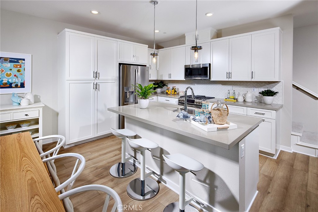 a kitchen with stainless steel appliances granite countertop a sink a stove a refrigerator and white cabinets with wooden floor