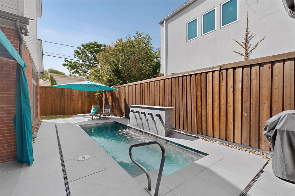 1526 Abrams Road Dallas, TX 75214 - Photo 31 of 38 Swimming pool with a multi-spout water feature, surrounded by light-toned pavers and a vertical wood fence