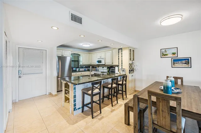 a kitchen with stainless steel appliances kitchen island granite countertop a dining table chairs and a refrigerator