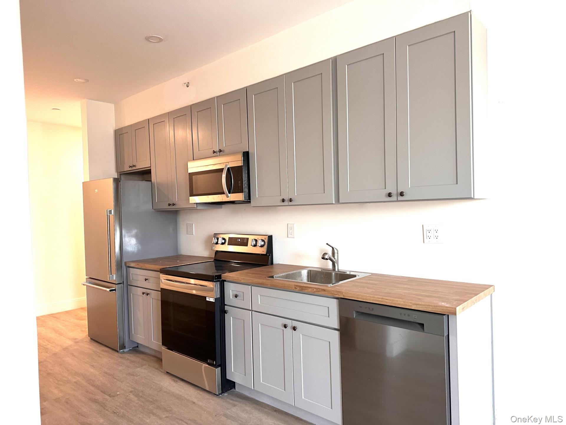 Kitchen with appliances with stainless steel finishes, light wood-type flooring, gray cabinets, butcher block countertops, and recessed lighting