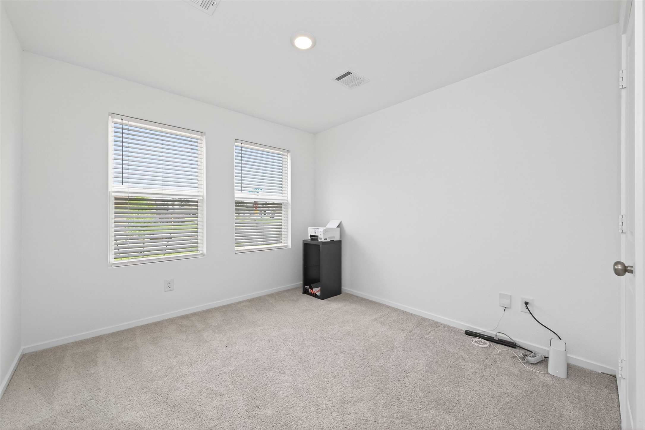 10720 Ellerston Road Cleveland, TX 77327 - Photo 17 of 32 This is a bright, carpeted room with neutral walls, featuring two windows for natural light. It has a small cabinet with office equipment, making it ideal for a home office or bedroom.