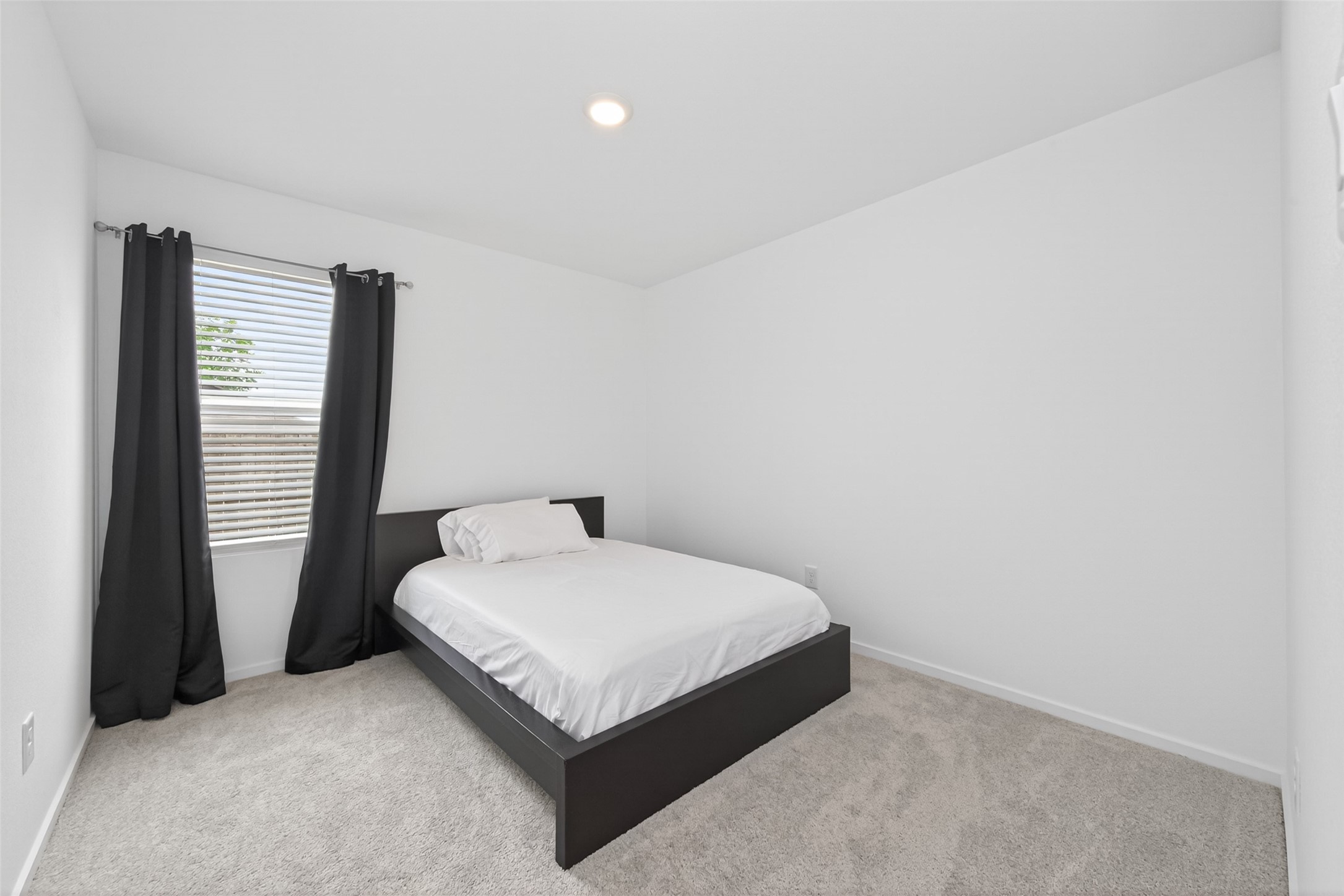 10720 Ellerston Road Cleveland, TX 77327 - Photo 18 of 32 This room is minimalistic and bright, featuring a single bed with white bedding, a window with black curtains, and soft carpeting.