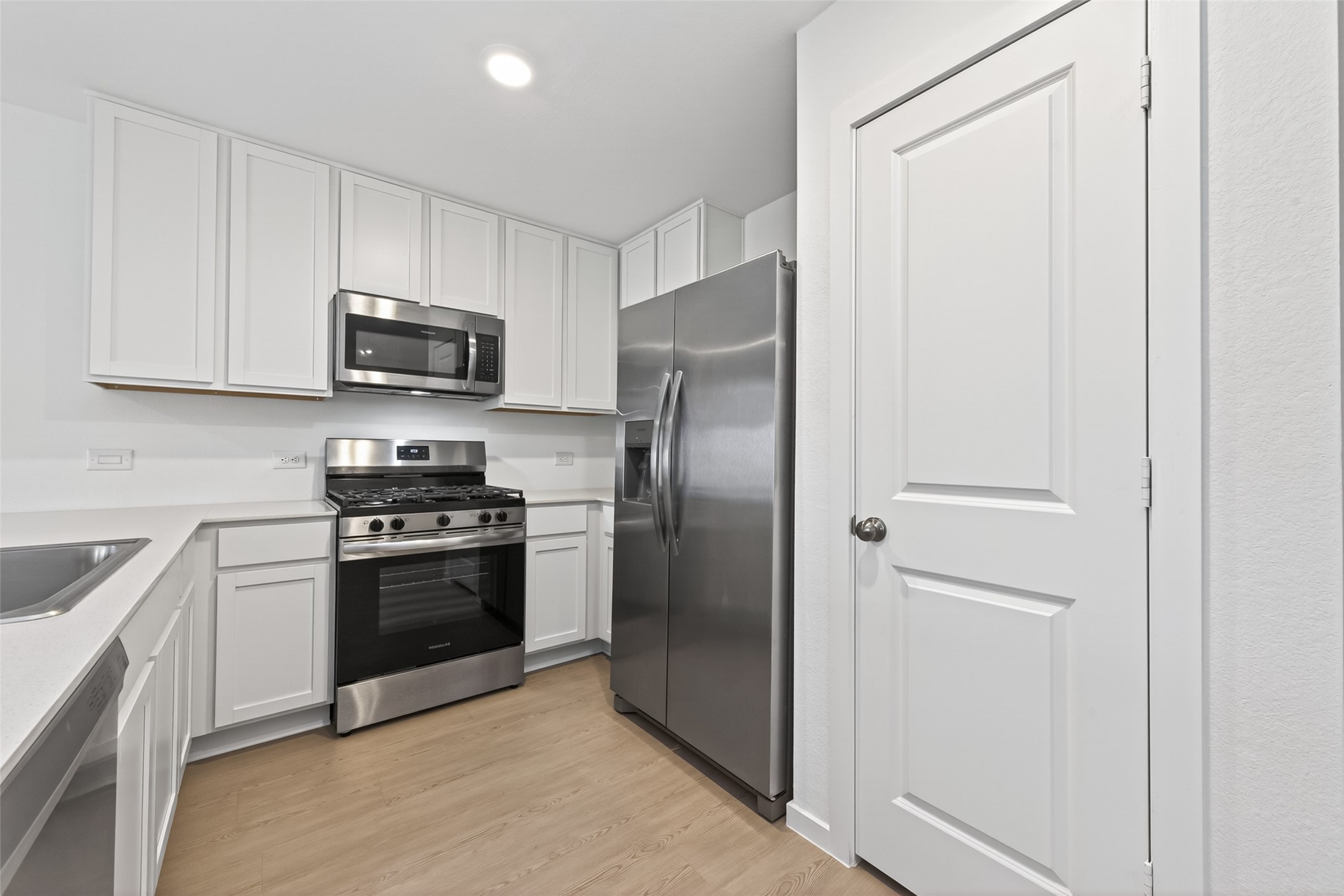 10720 Ellerston Road Cleveland, TX 77327 - Photo 5 of 32 This modern kitchen features sleek stainless steel appliances, white cabinetry, and light wood flooring, offering a clean and contemporary look.
