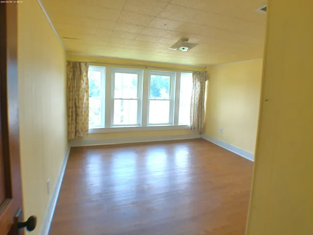 an empty room with wooden floor and windows with curtains