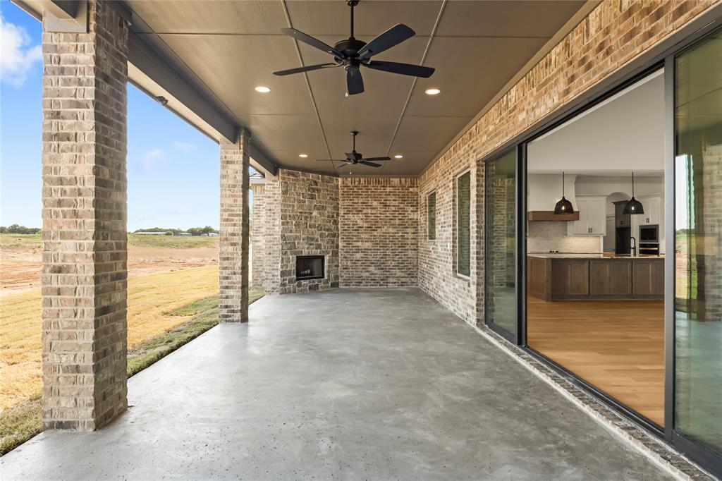 115 Red Bud Road Boyd, TX 76023 - Photo 33 of 38 Covered patio featuring a brick fireplace, dual ceiling fans, recessed lighting, and large sliding glass doors opening to an interior space with wood-finish flooring