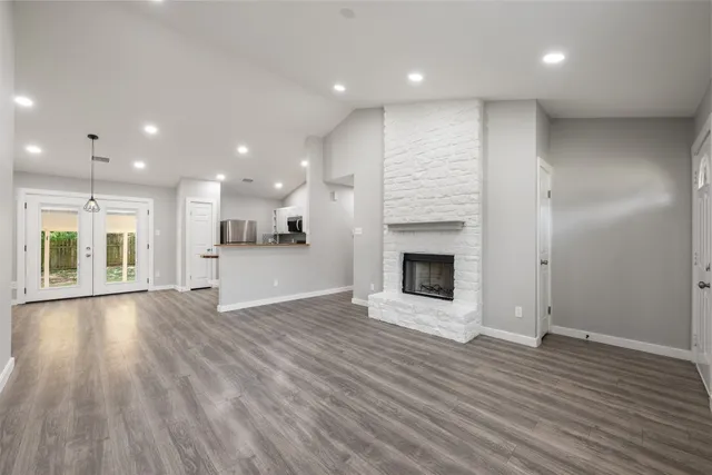 a view of an empty room with wooden floor and a kitchen