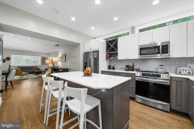 a kitchen with stainless steel appliances granite countertop a stove top oven a sink a refrigerator white cabinets and couches with wooden floor