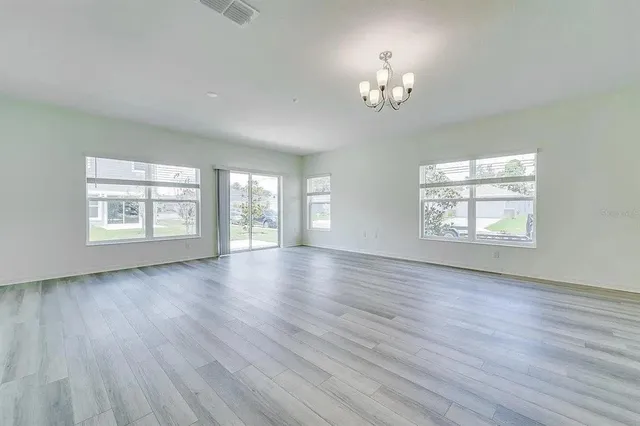 an empty room with wooden floor chandelier and windows