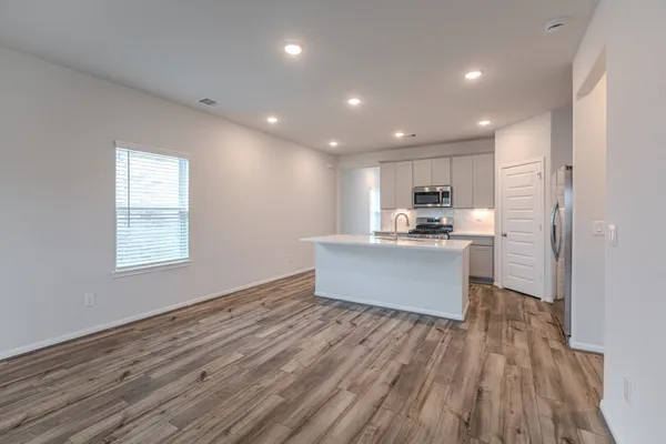 a large kitchen with kitchen island a sink wooden floor stainless steel appliances and white cabinets