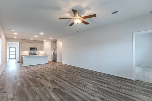 a view of an empty room with wooden floor and a kitchen