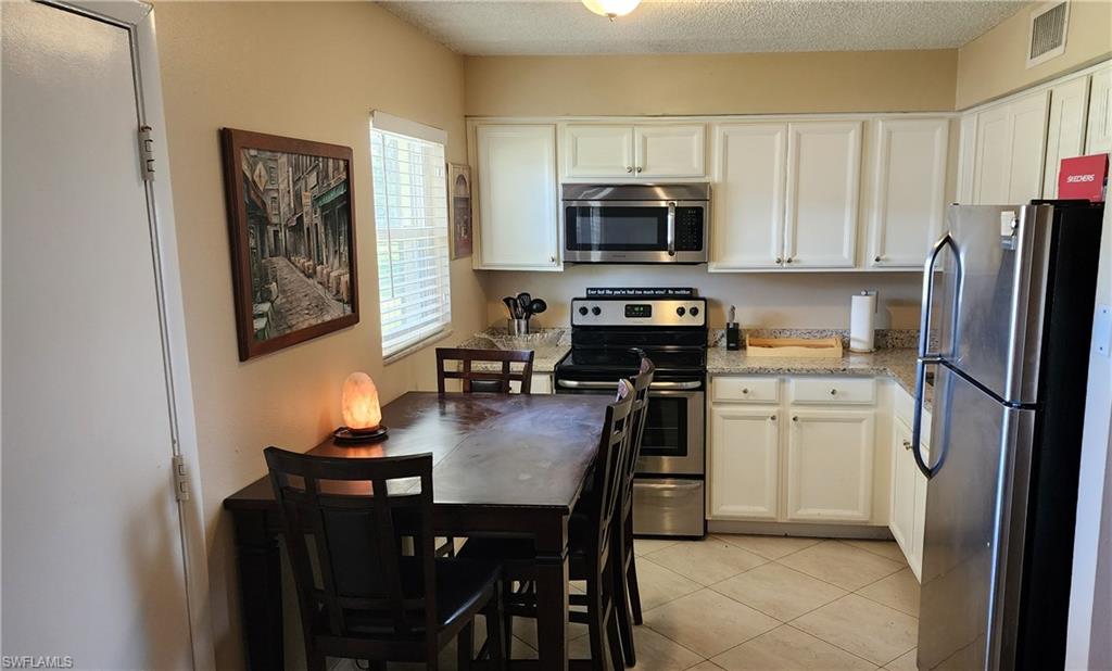 3325 Airport Road North, Unit J3 Naples, FL 34105 - Photo 4 of 13 a kitchen with stainless steel appliances a refrigerator a stove a sink a dining table and chairs