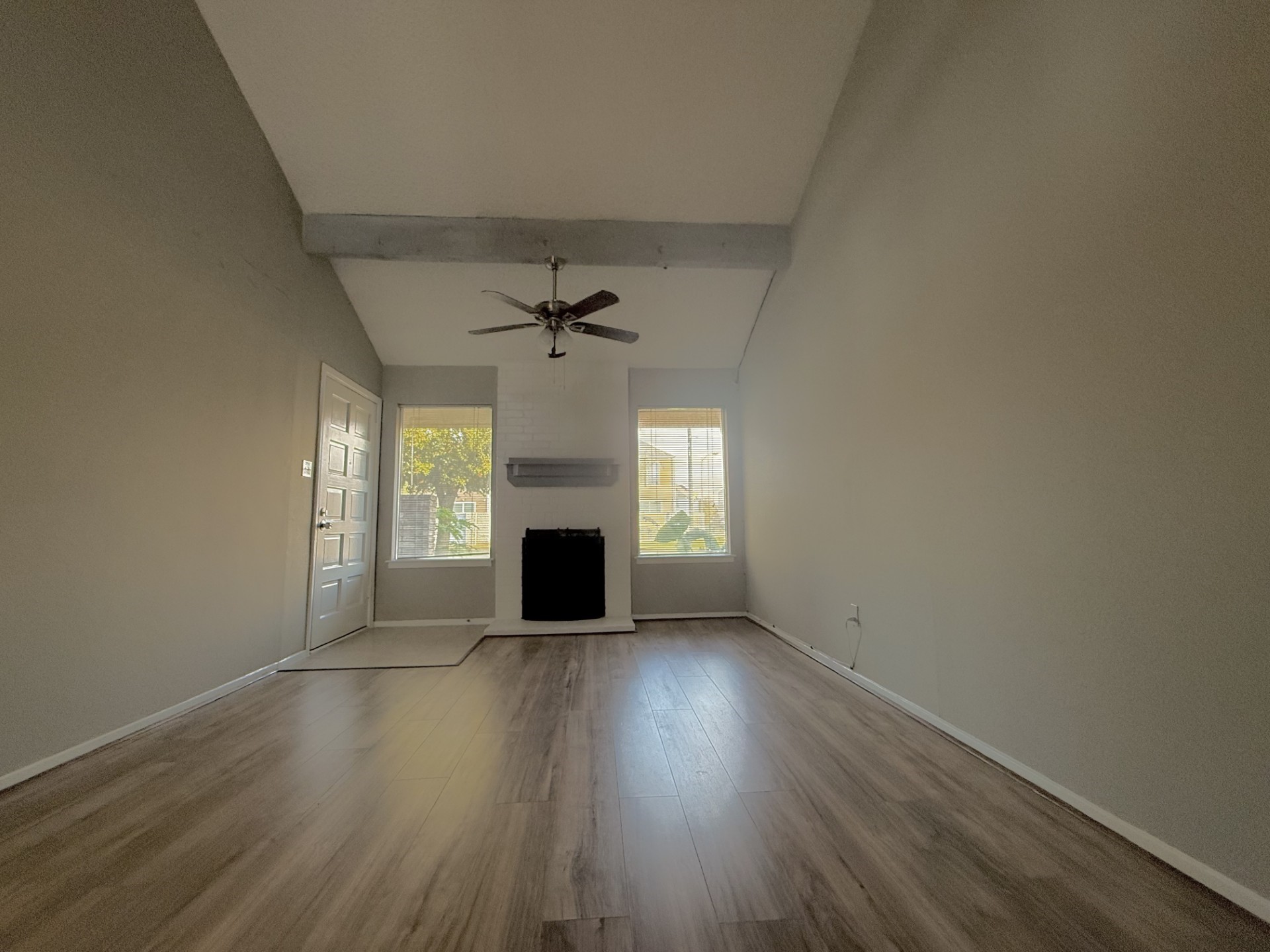 an empty room with wooden floor fireplace and windows