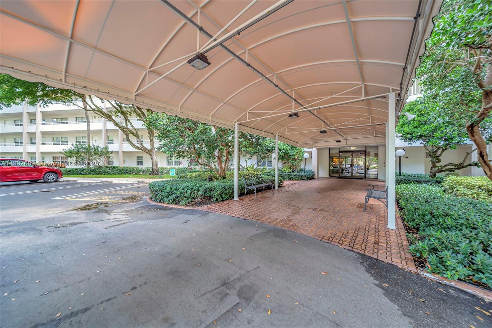3980 Oaks Clubhouse Drive, Unit 409 Pompano Beach, FL 33069 - Photo 49 of 70 Covered, convenient, and welcoming — the porte cochère entry offers shaded drop-off and easy access to the lobby, surrounded by mature landscaping and a well-kept building exterior.