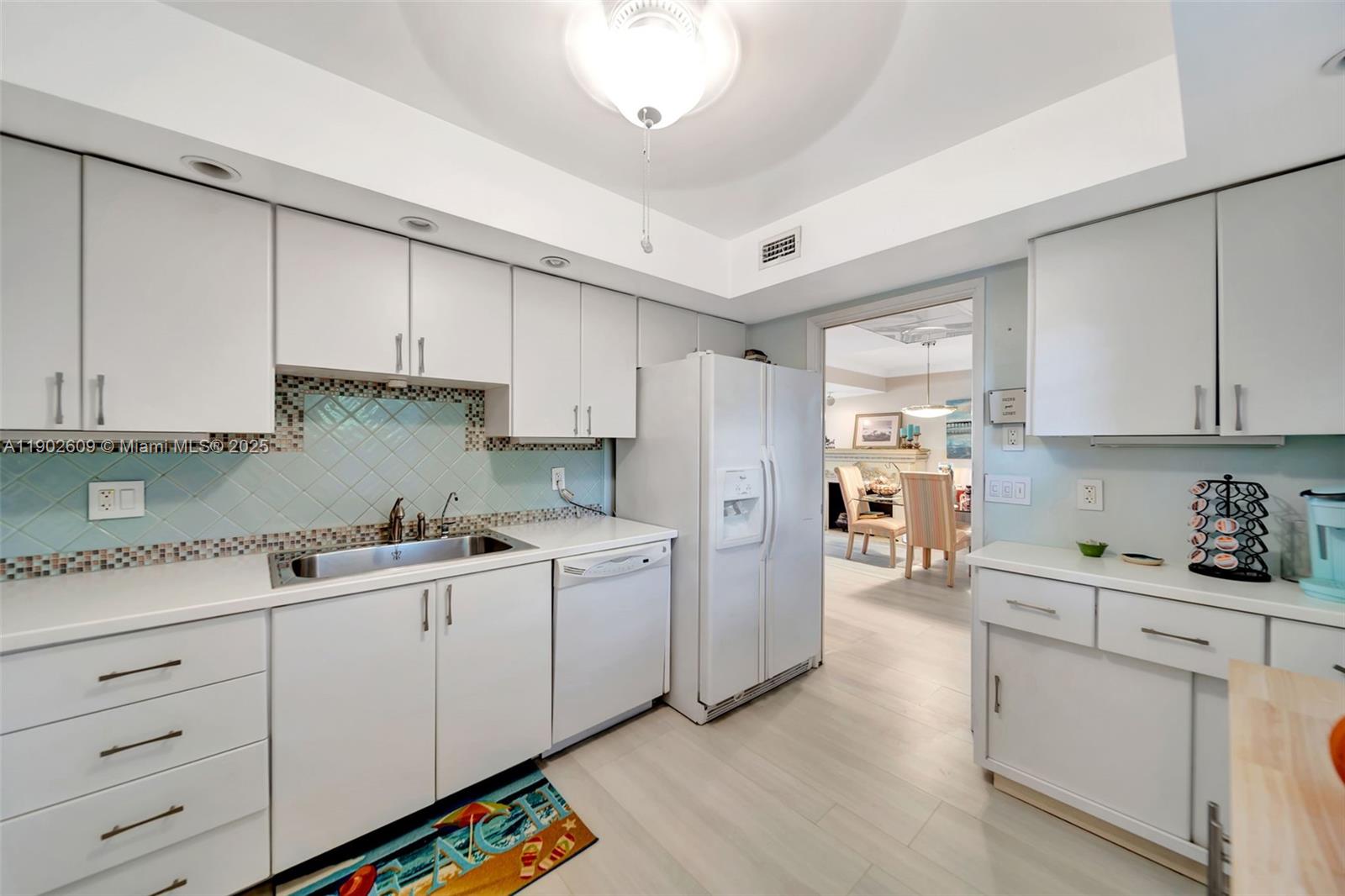 3980 Oaks Clubhouse Drive, Unit 409 Pompano Beach, FL 33069 - Photo 5 of 70 Light, bright, and functional — this kitchen offers extensive cabinet storage, clean white finishes, tile backsplash with accent detailing, and direct access to the dining area for easy entertaining.